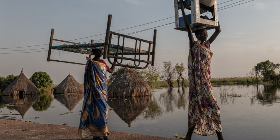 南蘇丹團結州的洪水中，婦女們扛著家具行走。洪水將當地人的農作和牲畜淹沒，嚴重衝擊他們的生計。